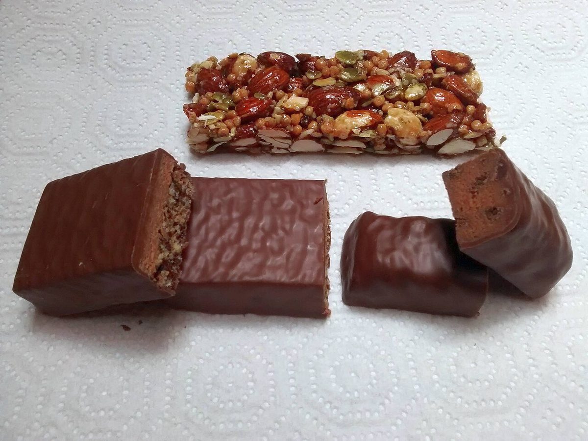 Trzy batony proteinowe, dwa w czekoladowej polewie przekrojone na pół i jeden z orzechów i pestek