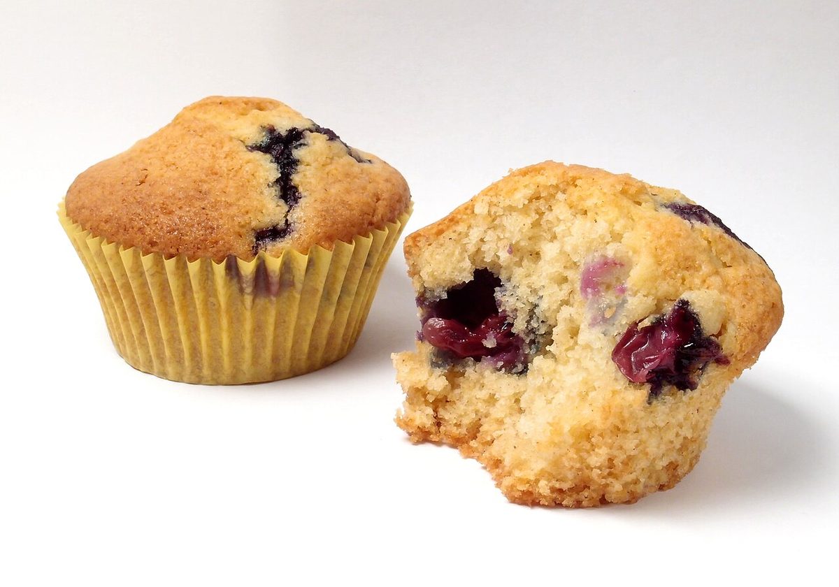 Dwie muffinki z borówkami, jedna w papilotce, druga przełamana z widocznymi owocami