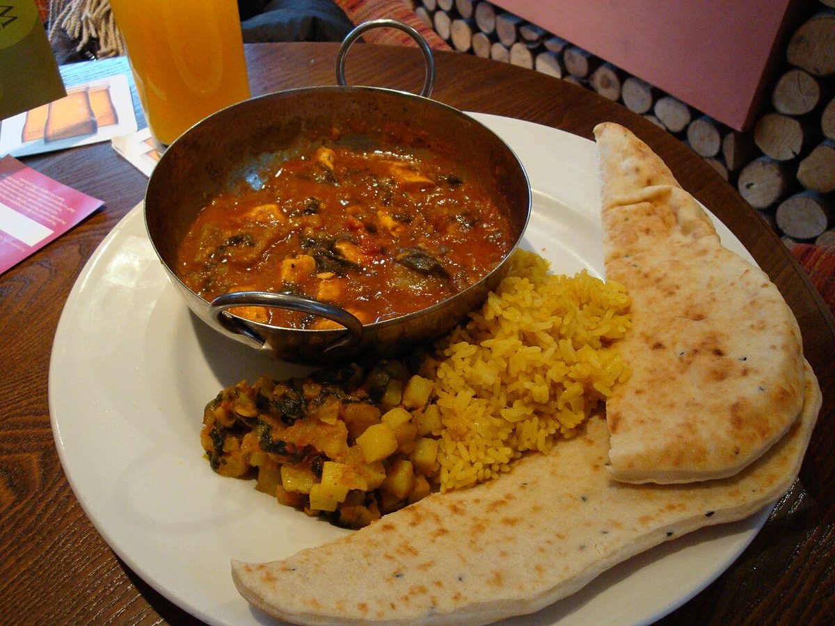 Curry z kurczakiem i soczewicą w metalowej miseczce z ryżem i chlebkiem naan na talerzu