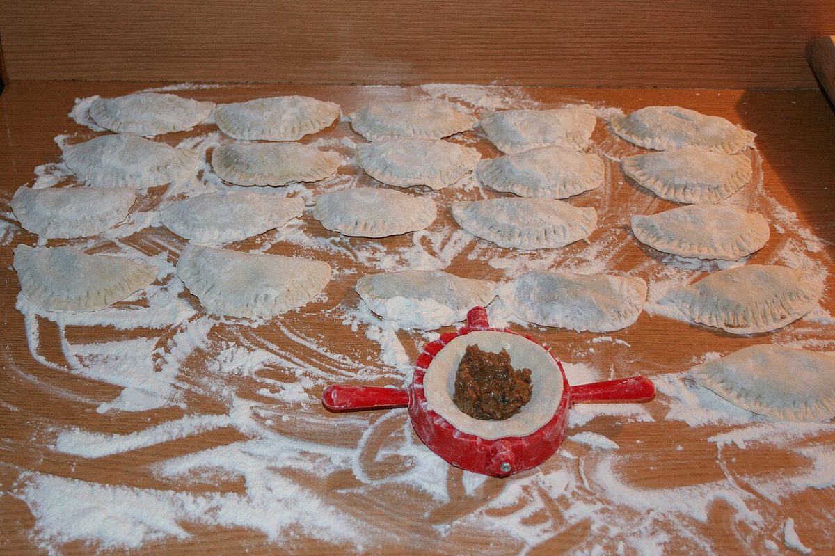 Ulepione surowe pierogi ułożone na oprószonej mąką stolnicy z miseczką farszu