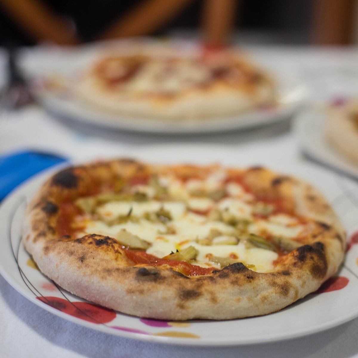 Pizza z mozzarellą i sosem pomidorowym na talerzu, w tle druga pizza